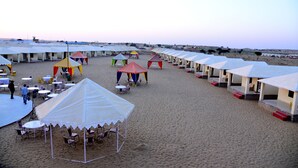 A beachside resort with multiple tents and tables, some with umbrellas.
