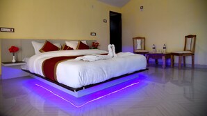 A modern hotel room with a large bed, bedside tables, a mirror, and a small table with a chair.