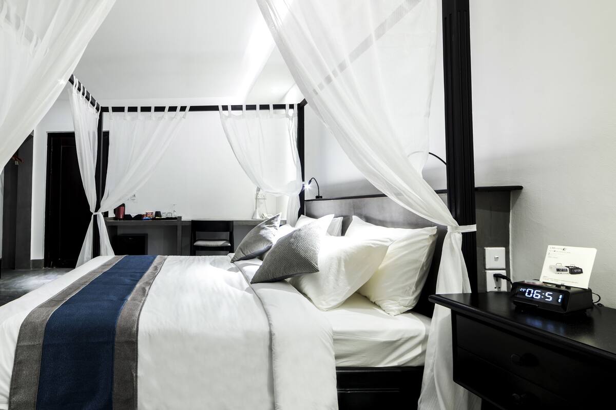 A modern hotel room with a bed, a bedside table, a desk, and a TV.