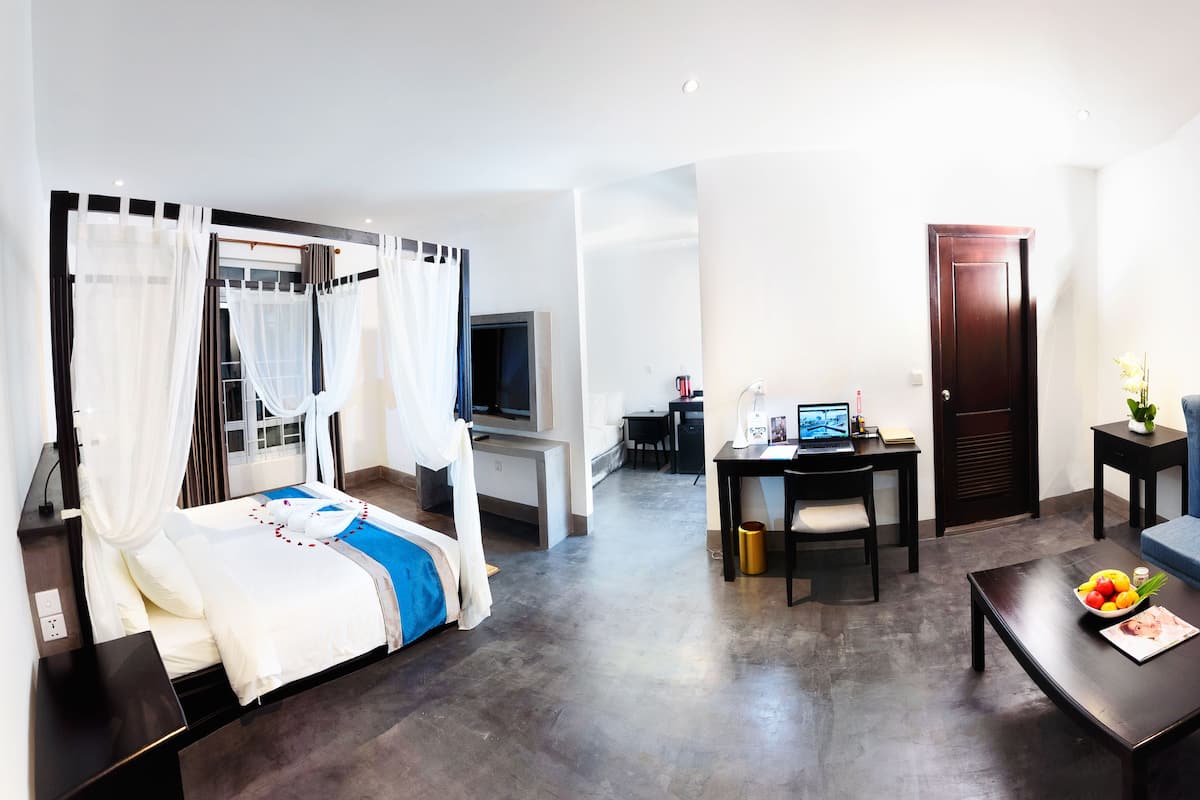A hotel room with a bed, a sofa, a coffee table, a desk with a computer, and a TV.