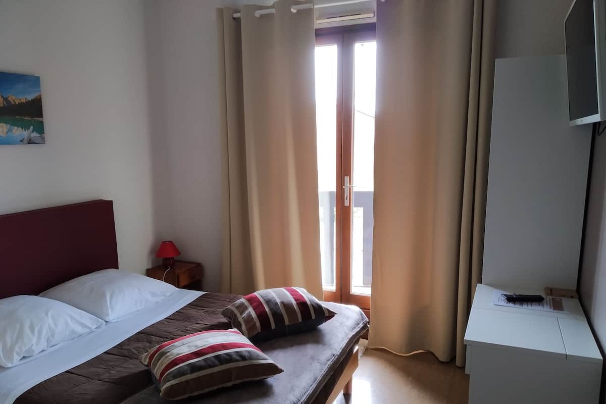 Hotelkamer met een bed, kussens, een nachtkastje met lamp, een bureau met stoel en een raam met gordijnen.