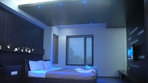 A modern bedroom with a bed, a TV, and a window with blinds. - Hotel Kanan (Gandhinagar)