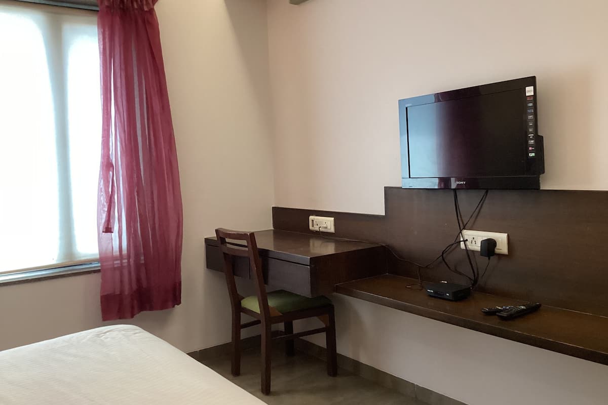A hotel room with a bed, a desk with a chair, a television mounted on the wall, and a window with a curtain.