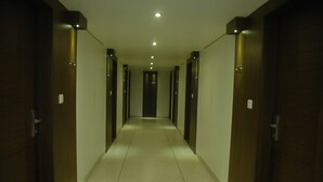 A long, narrow hallway with wooden doors on either side and a tiled floor. - Hotel Kanan (Gandhinagar)