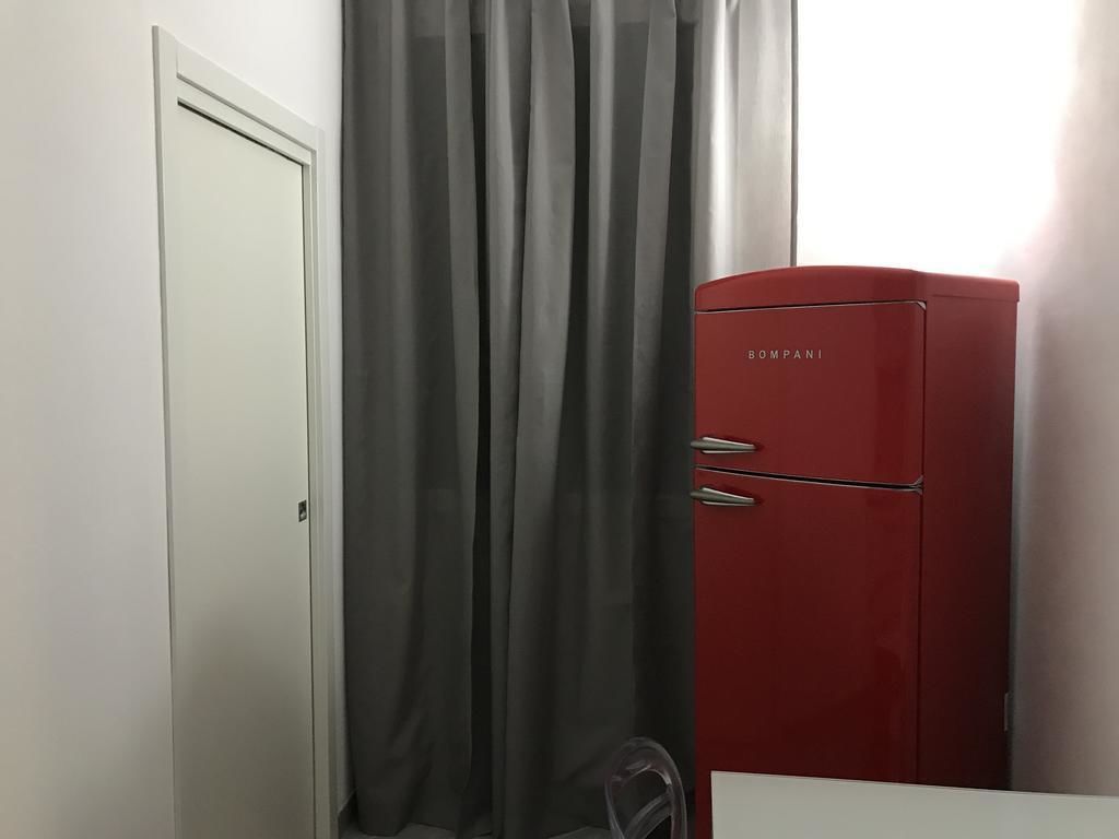 A room with a closed door, a red refrigerator, and a curtain.