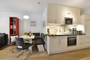 A modern kitchen with white cabinets, a built-in oven, and a microwave. There is a dining area with a bench and a red bookshelf. - Starfish - starfish in Ostseebad Breege OT Juliusruh auf Rügen (Breege)