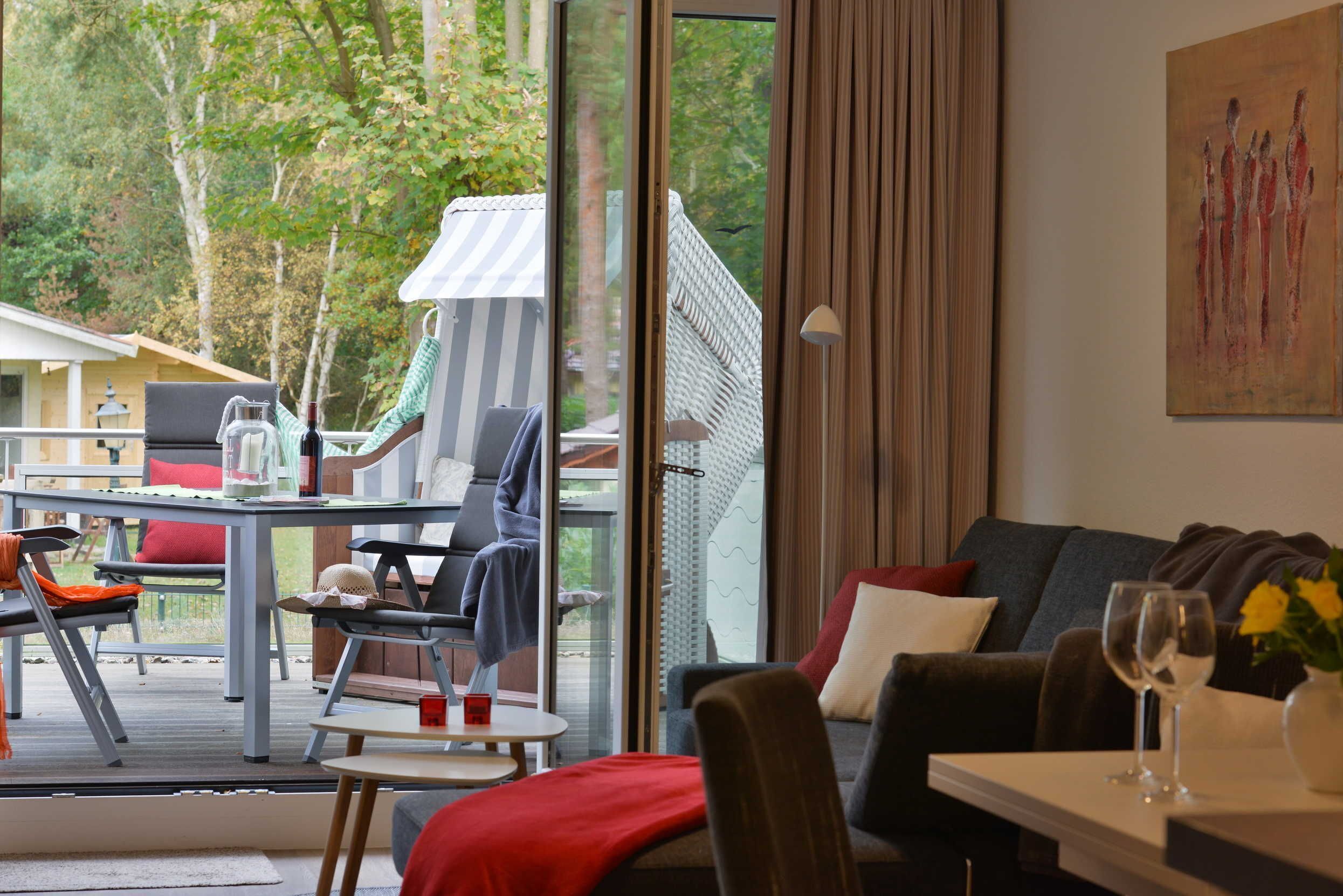 En moderne stue med en glasdør, der fører til en terrassemiljø, et spiseområde med bord og stole, og en hyggelig siddekrog med sofa og puder.
