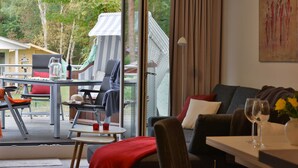 Un soggiorno moderno con una porta vetrata che dà su una terrazza esterna, un’area pranzo con tavolo e sedie, e un angolo salotto accogliente con divano e cuscini.