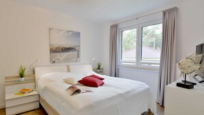 Una camera da letto ordinata con un letto grande, un comodino con una lampada, una piccola pianta e una finestra con tende.