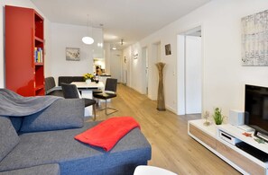A modern living room with a grey sofa, a red bookshelf, and a flat-screen TV on a white console. - Starfish - starfish in Ostseebad Breege OT Juliusruh auf Rügen (Breege)