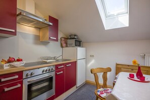 Une cuisine de taille réduite avec des meubles rouges, une cuisinière en acier inoxydable et un four à micro-ondes posé sur le plan de travail.