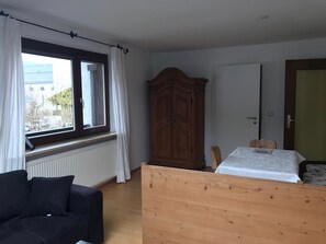 Une chambre à coucher avec un lit en bois, une fenêtre avec des rideaux, un radiateur, une armoire et une porte.