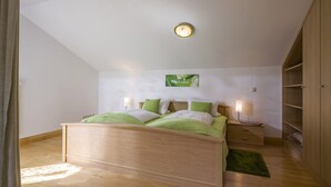 Ein Schlafzimmer mit einem hölzernen Bett, Bettwäsche in Grün und Weiß, einer Wanduhr, einem Nachttisch mit einer Lampe und einem grünen Teppich.