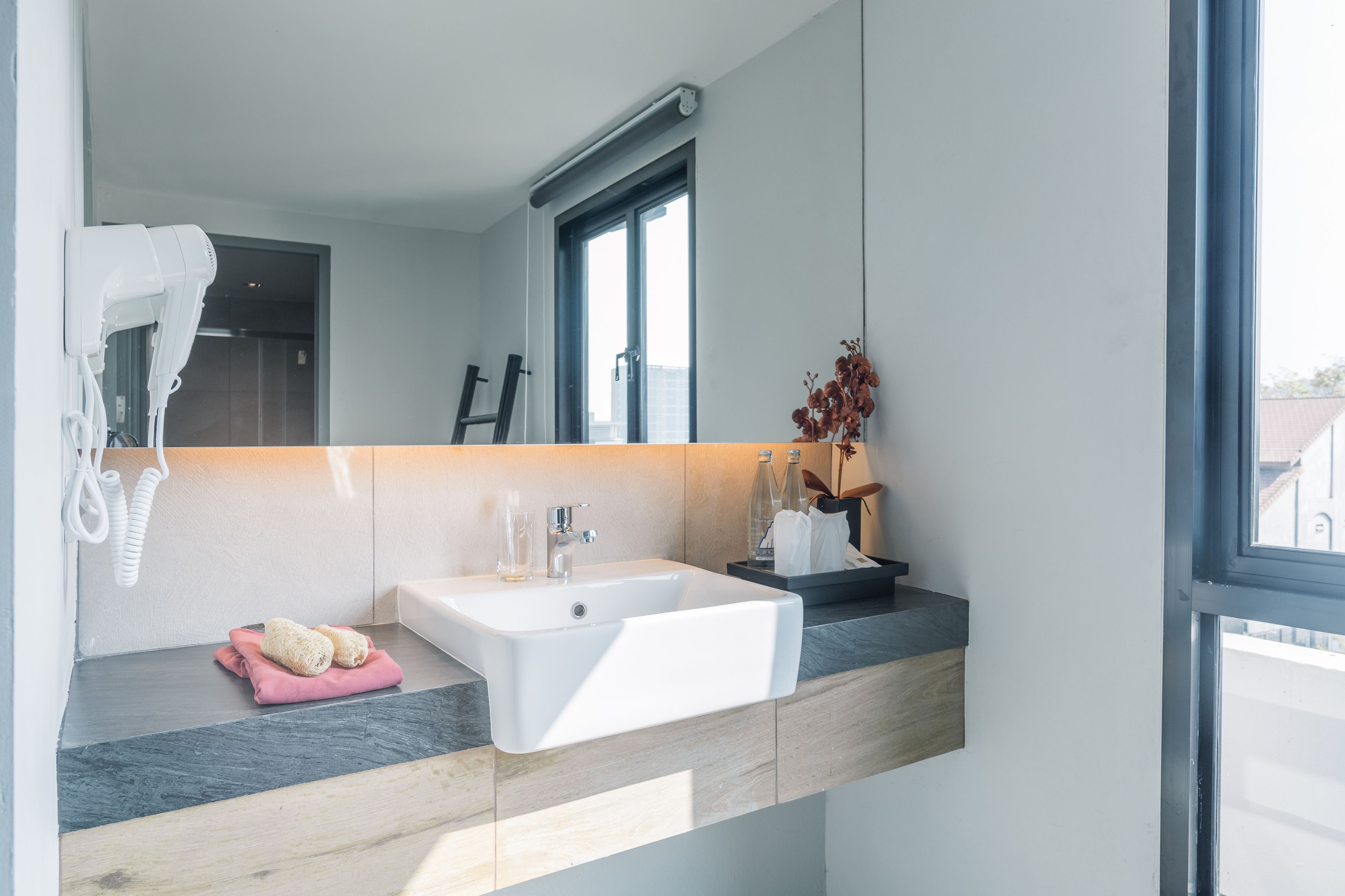 A modern bathroom with a large mirror, a white sink, and a hairdryer mounted on the wall.