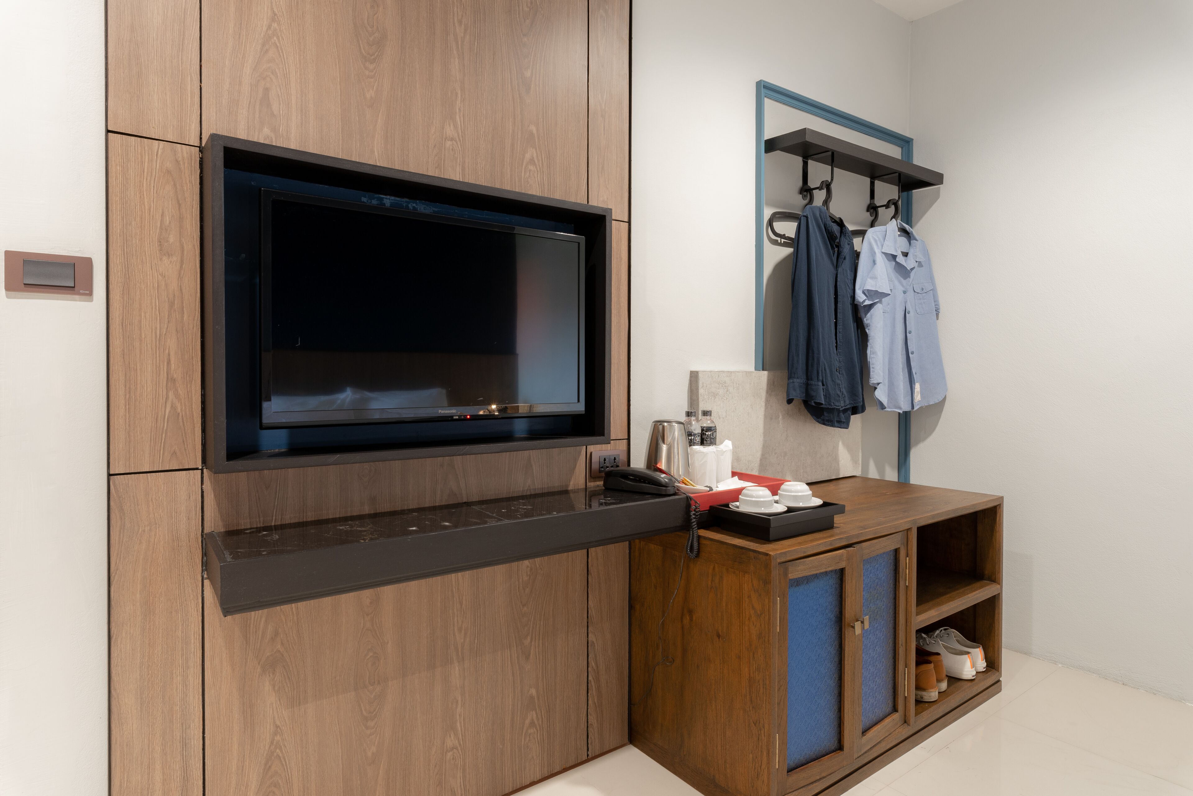 A modern bathroom with a wooden vanity, a built-in TV, a mirror, and a clothing rack.