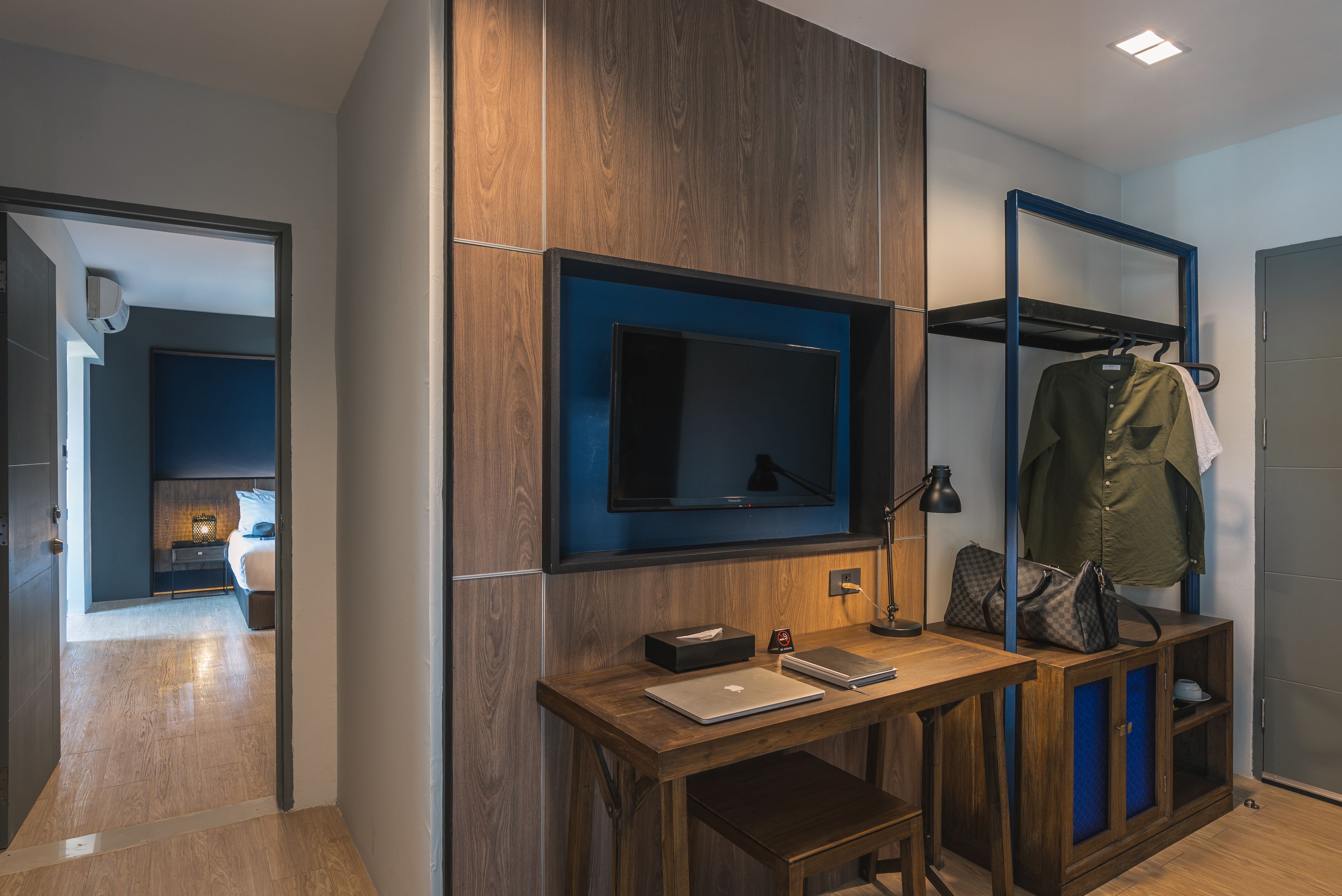 A modern hotel room with a wooden desk, a flat-screen TV, a coat rack, and a wardrobe.