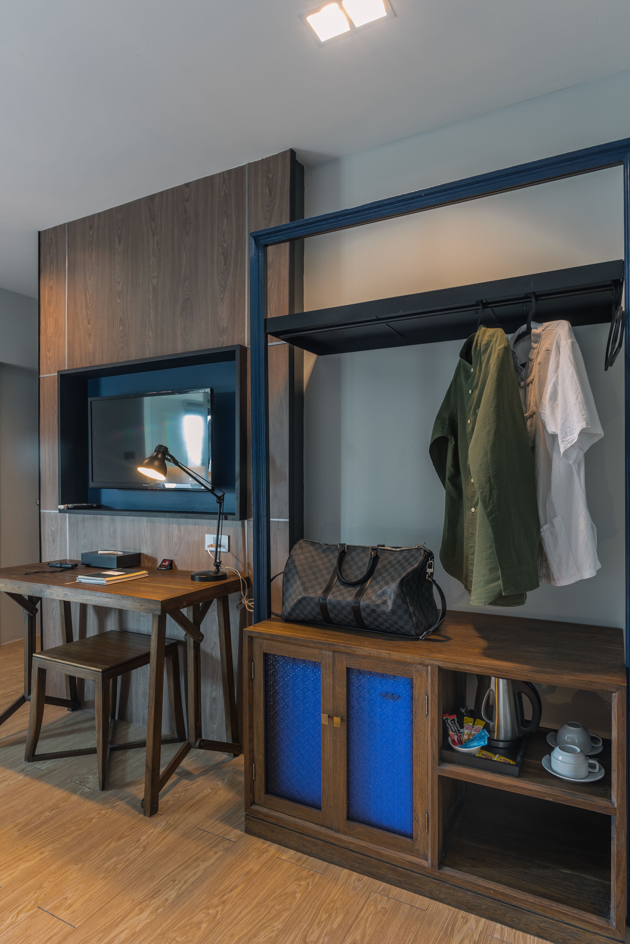 Een kamer met een houten bureau, een aan de muur bevestigde televisie, een kapstok en een kast met een blauw interieur.