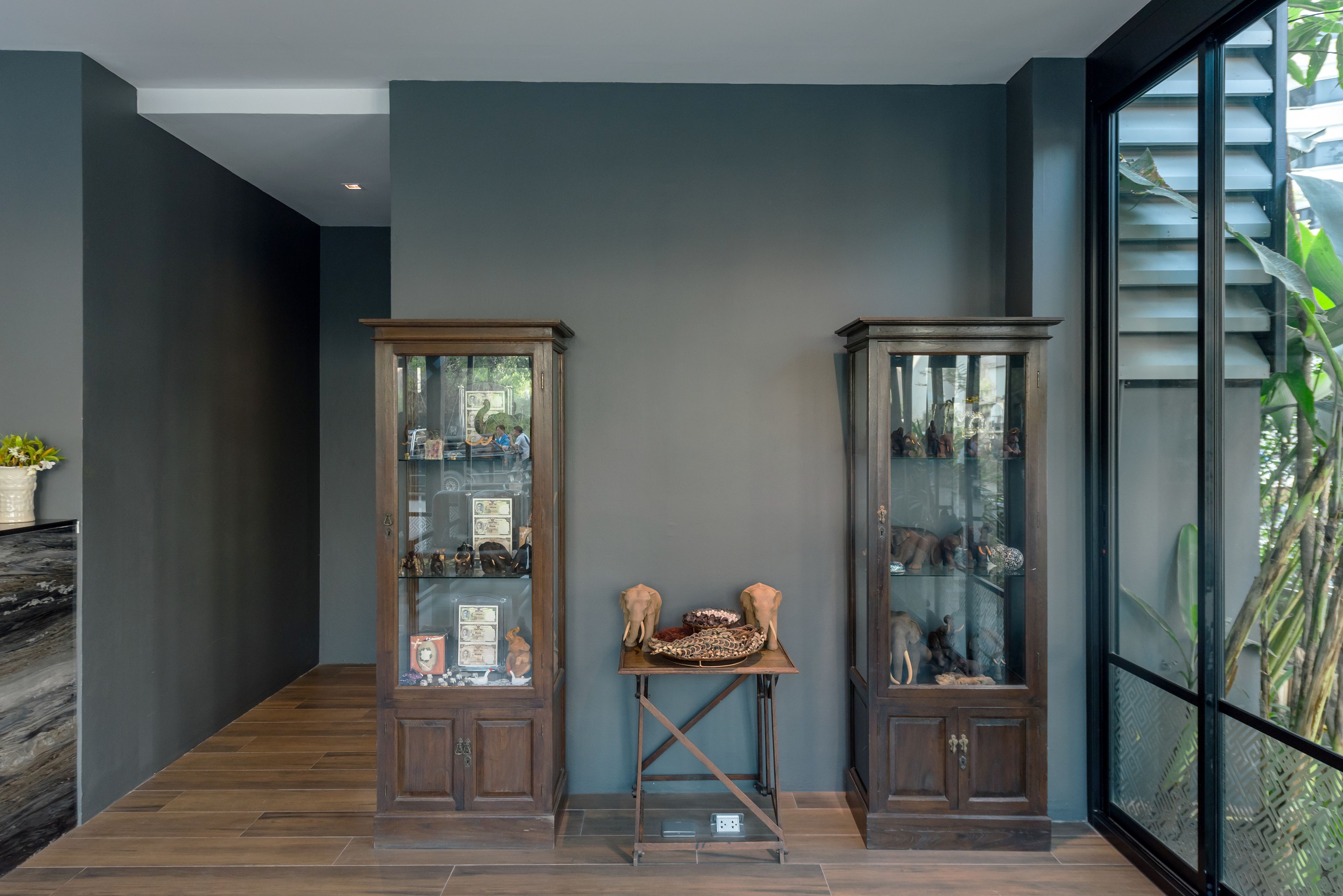 A hallway with dark walls and wooden flooring, flanked by two glass-fronted cabinets with various items displayed inside.