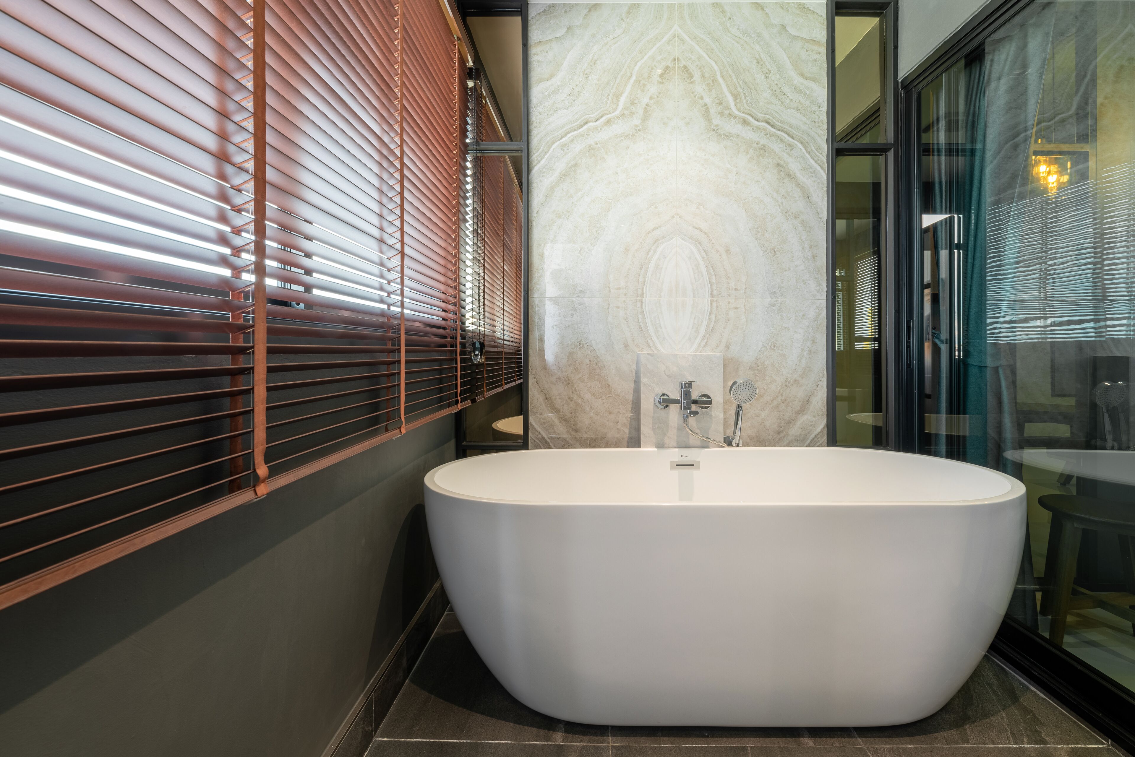A modern bathroom with a freestanding bathtub, a glass shower enclosure, and a marble wall.