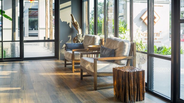 Un moderno vestíbulo de hotel con amplios ventanales, suelo de madera y una zona de estar con un sofá y sillones.