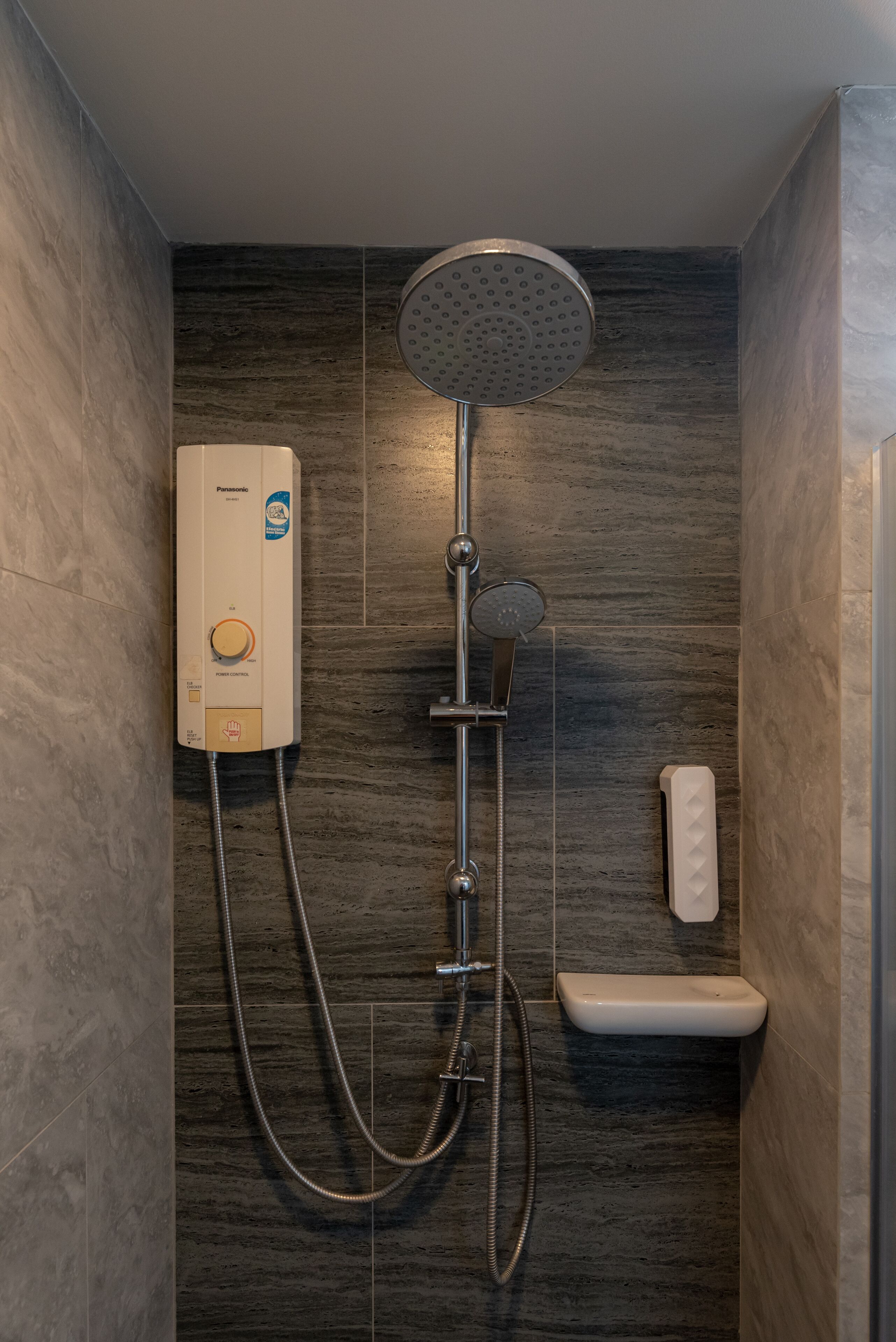 Una ducha moderna con cabezal de ducha manual, panel de control en la pared y manguera de ducha.