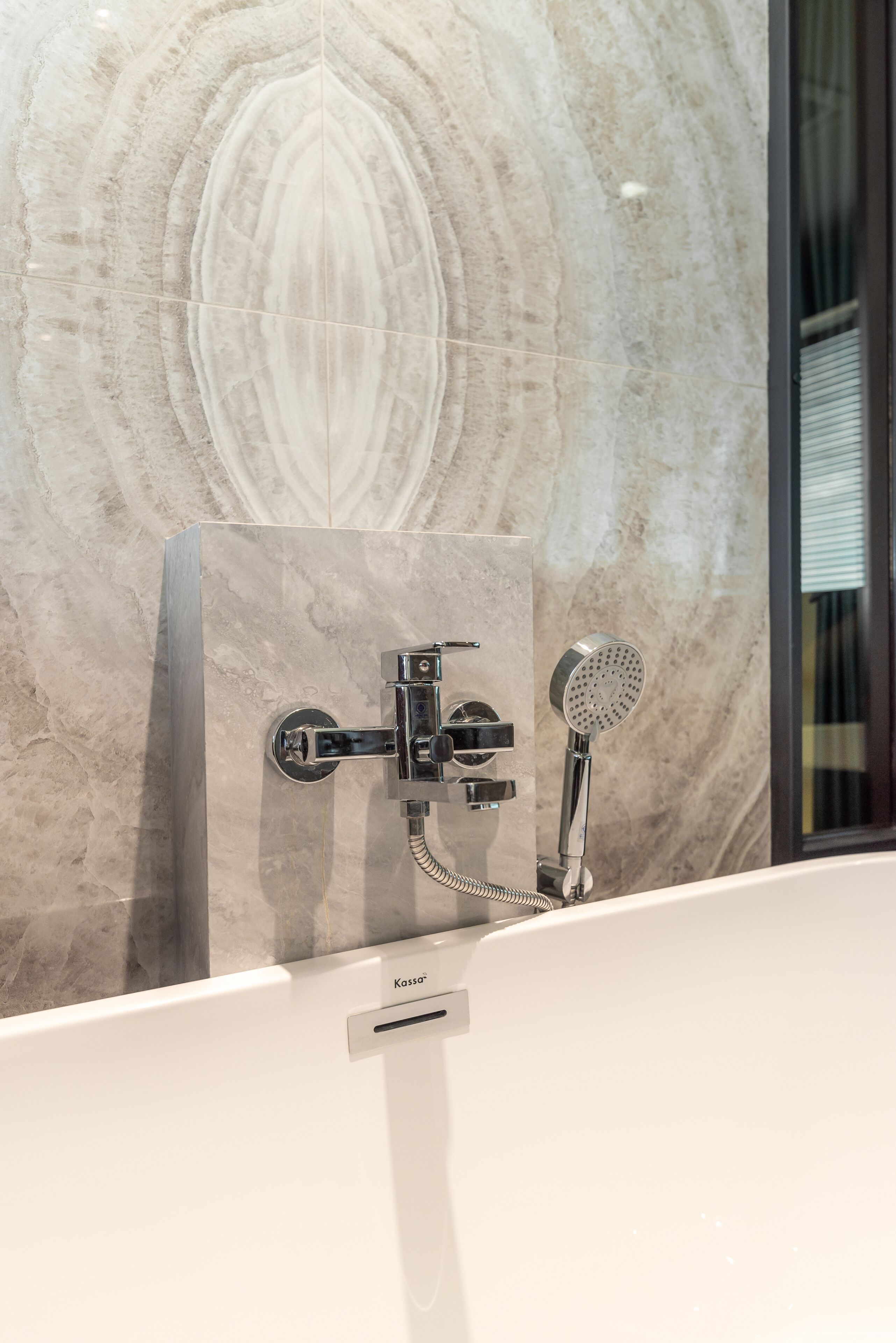 A modern bathroom with a marble wall, a built-in bathtub, and a handheld showerhead.