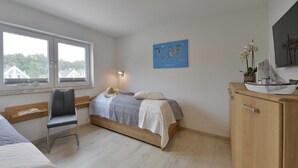 Une chambre à coucher avec un lit, une chaise, un bureau, une carte accrochée au mur et une maquette de bateau posée sur une commode.