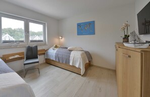 Quarto com cama, uma cadeira, escrivaninha, mapa na parede e modelo de navio em um armário.