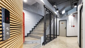 A modern interior with a staircase, a wall-mounted elevator, and a door with a number sign. - Rest24 Residence (Bangkok)
