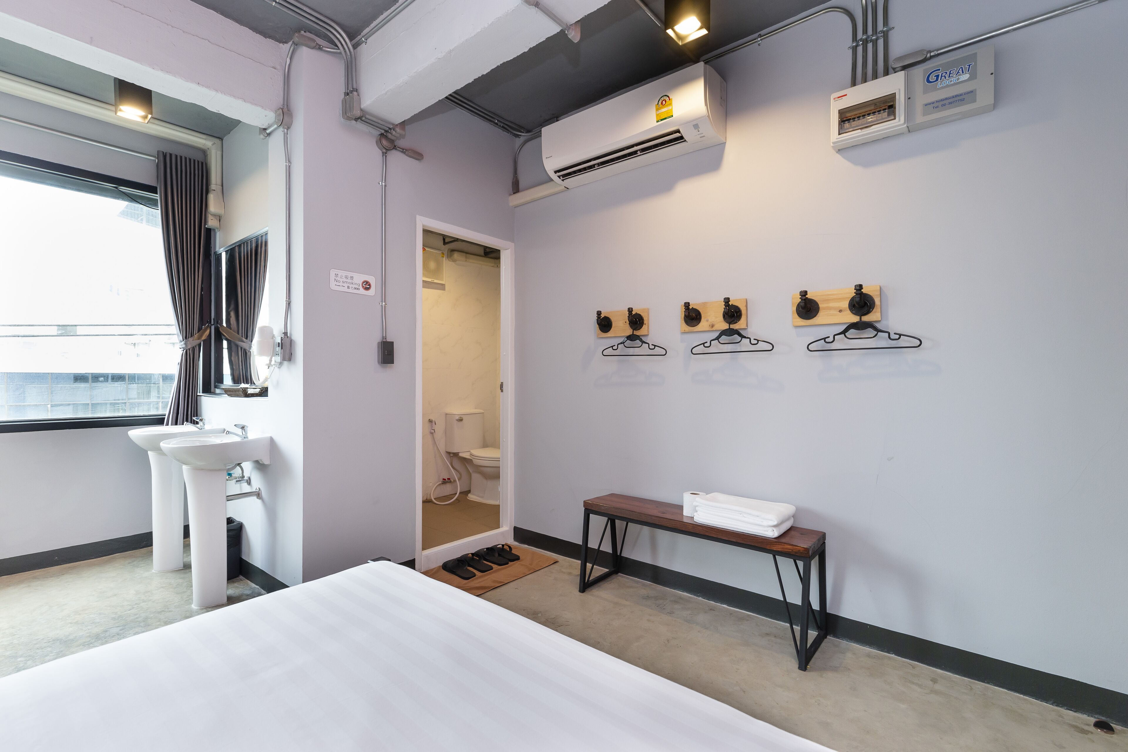 Une chambre d’hôtel avec un lit, deux lavabos, un banc avec des serviettes, un appareil de climatisation et une vue sur l’extérieur.