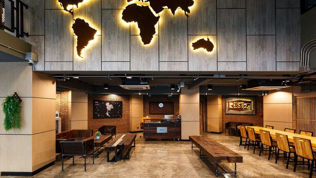 A modern restaurant with a wooden wall, a world map, and a long dining table with chairs. - Rest24 Residence (Bangkok)