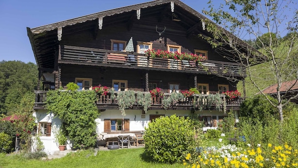 A traditional wooden chalet with multiple balconies, a garden with flowers, and a clear blue sky. - 6 people Apartment / Auerbach (Oberaudorf)
