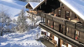 A wooden chalet with a balcony, surrounded by snow-covered trees and a clear sky. - 6 people Apartment / Auerbach (Oberaudorf)