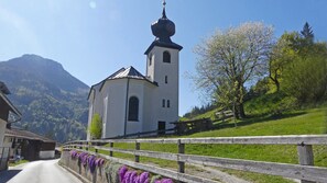 En hvid kirke med et kirketårn, omgivet af et træhegn og lilla blomster.