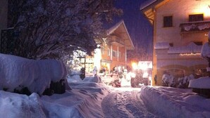 A snow-covered street with buildings on either side, including a visible sign for a restaurant. - Apartment in the house Heidinger (Oberaudorf)