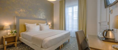 A hotel room with a large bed, a desk, a chair, a television, and a patterned floor.