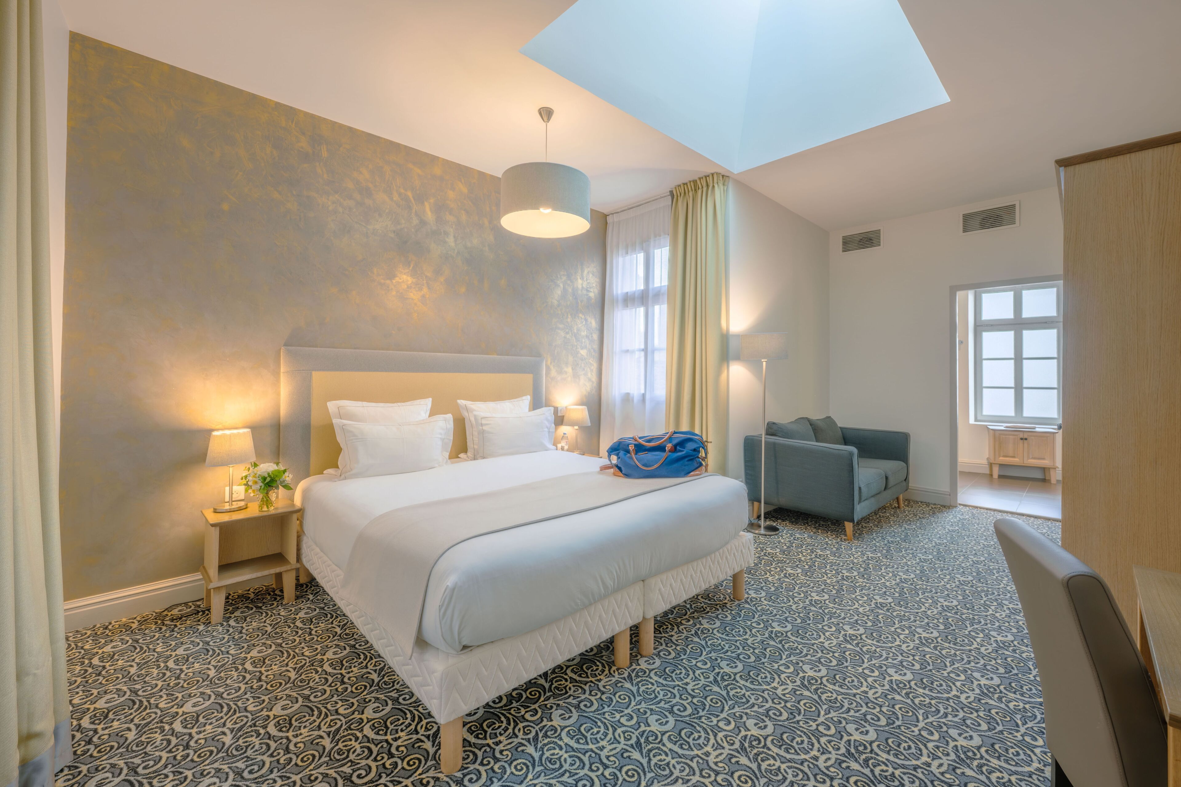 A hotel room with a large bed, a sitting area with a sofa, a desk, and a window with curtains.