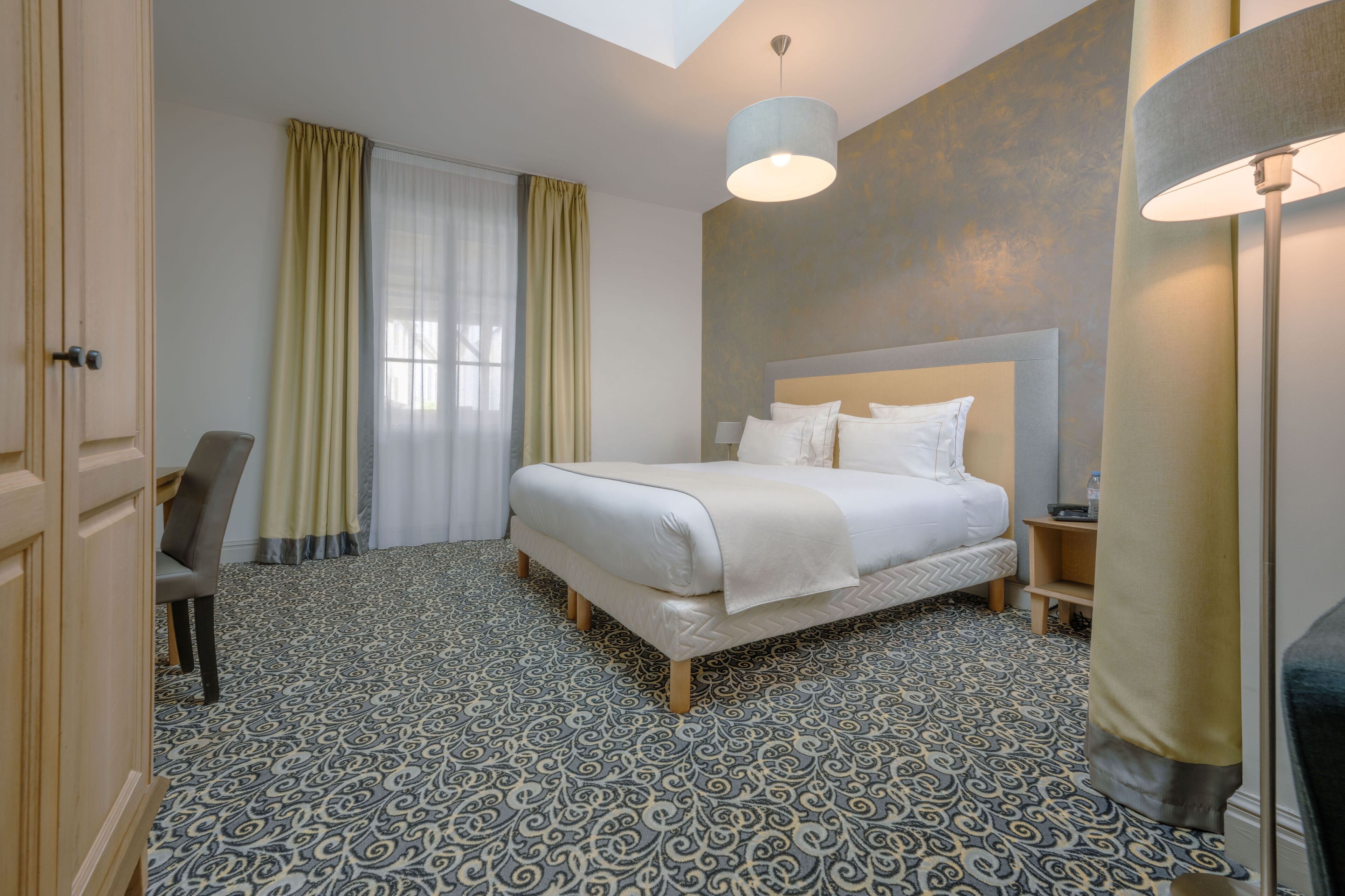 Een hotelkamer met een bed, een stoel, een nachtkastje, een lamp en een kamer met vloerkleed.