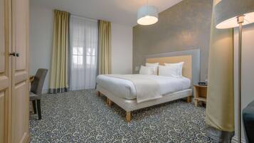 Een hotelkamer met een bed, een stoel, een nachtkastje, een lamp en een kamer met vloerkleed.