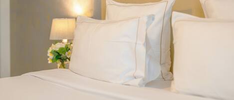 A neatly made bed with white linens and pillows, a bedside lamp, and a vase with flowers.