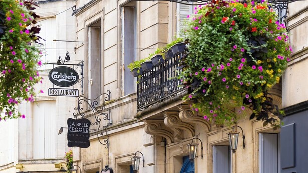 Una calle con mesas al aire libre, un café llamado 'Carlsberg Restaurant', y un edificio con puerta azul y un letrero que dice 'La Belle Epoque'.