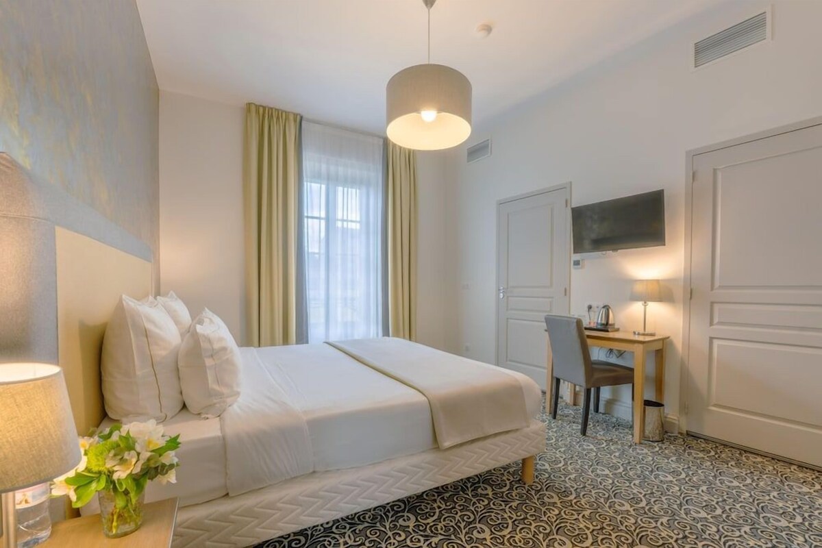 A hotel room with a bed, a desk, a chair, a television, and a patterned floor.