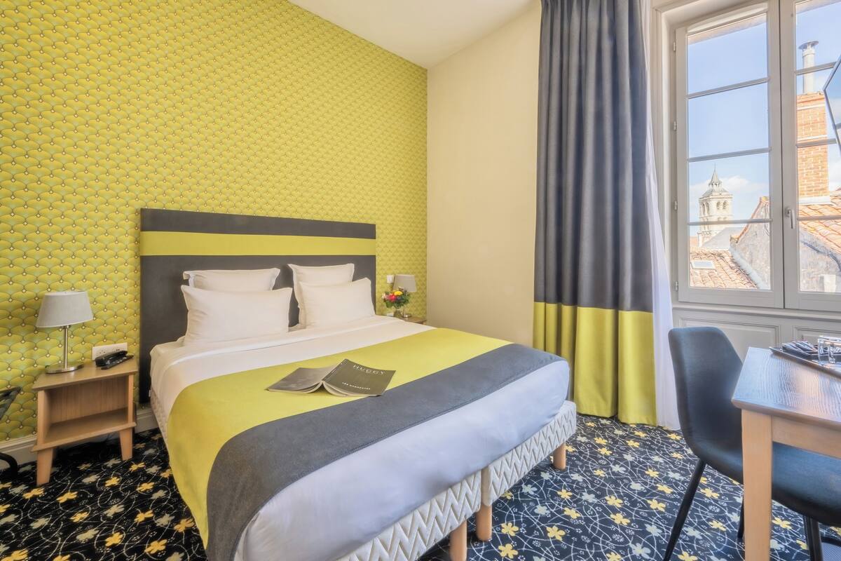 Una habitación de hotel con cama, escritorio y ventana con vistas a edificios.