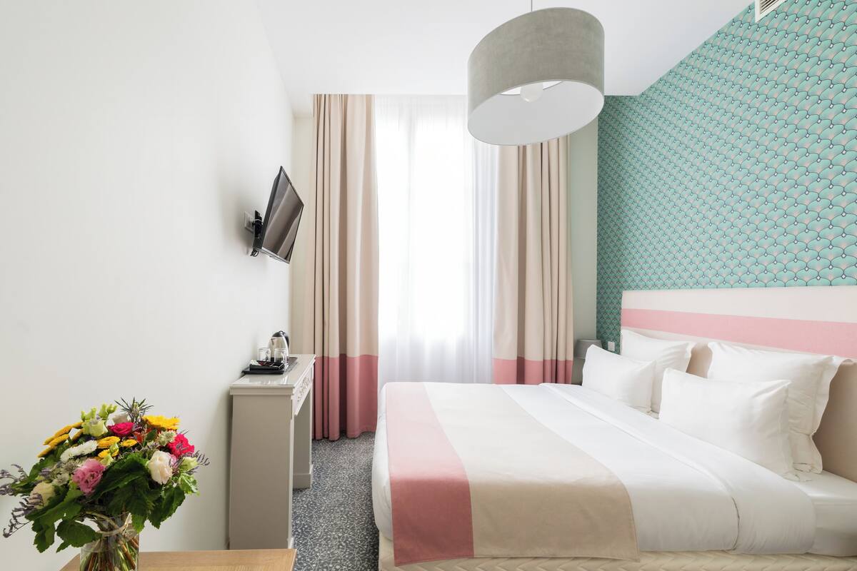 Una habitación de hotel con cama, escritorio, televisión y ventana con cortinas.