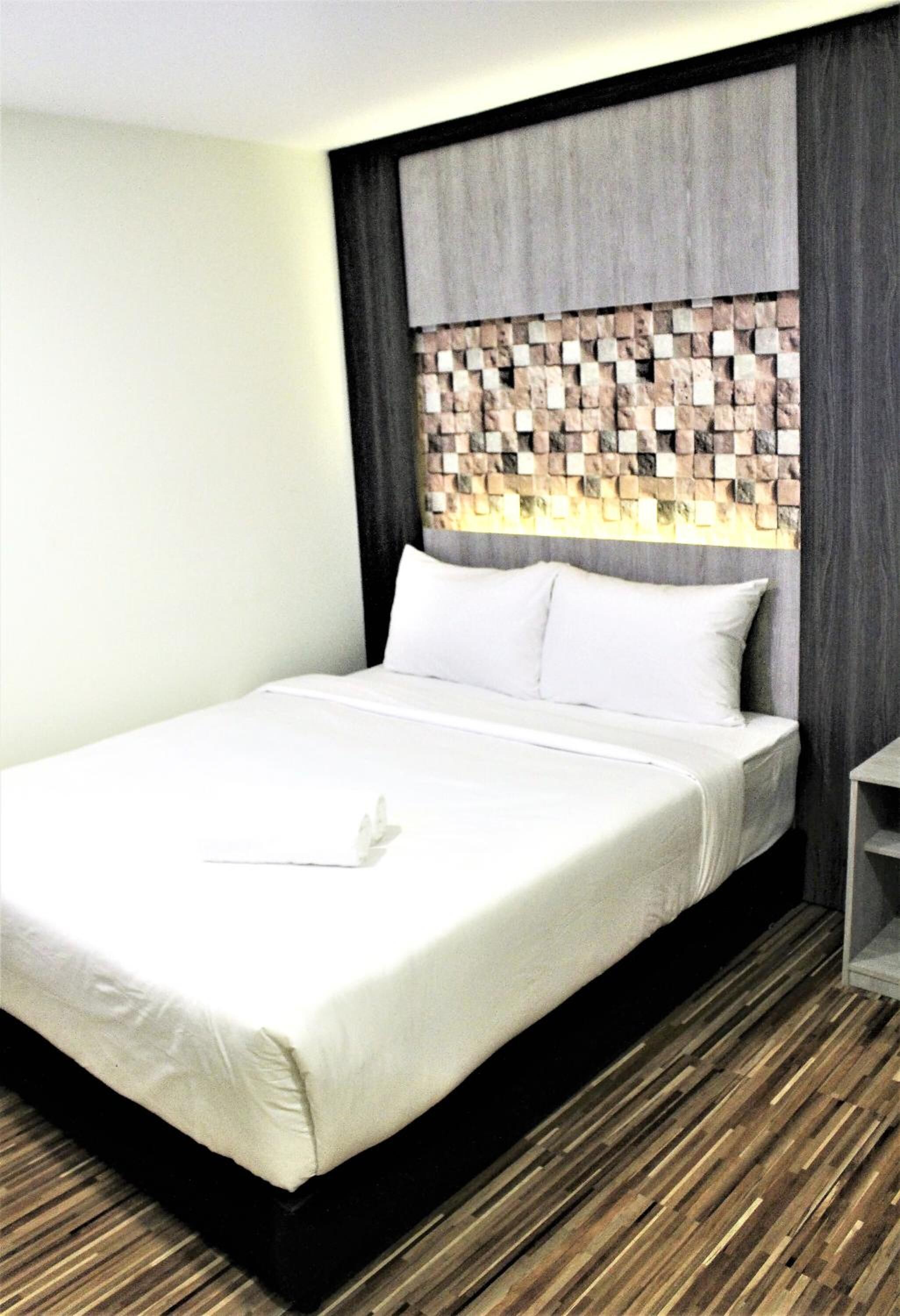 A neatly made bed with white linens and pillows, a wooden headboard with a patterned design, and a wooden floor.