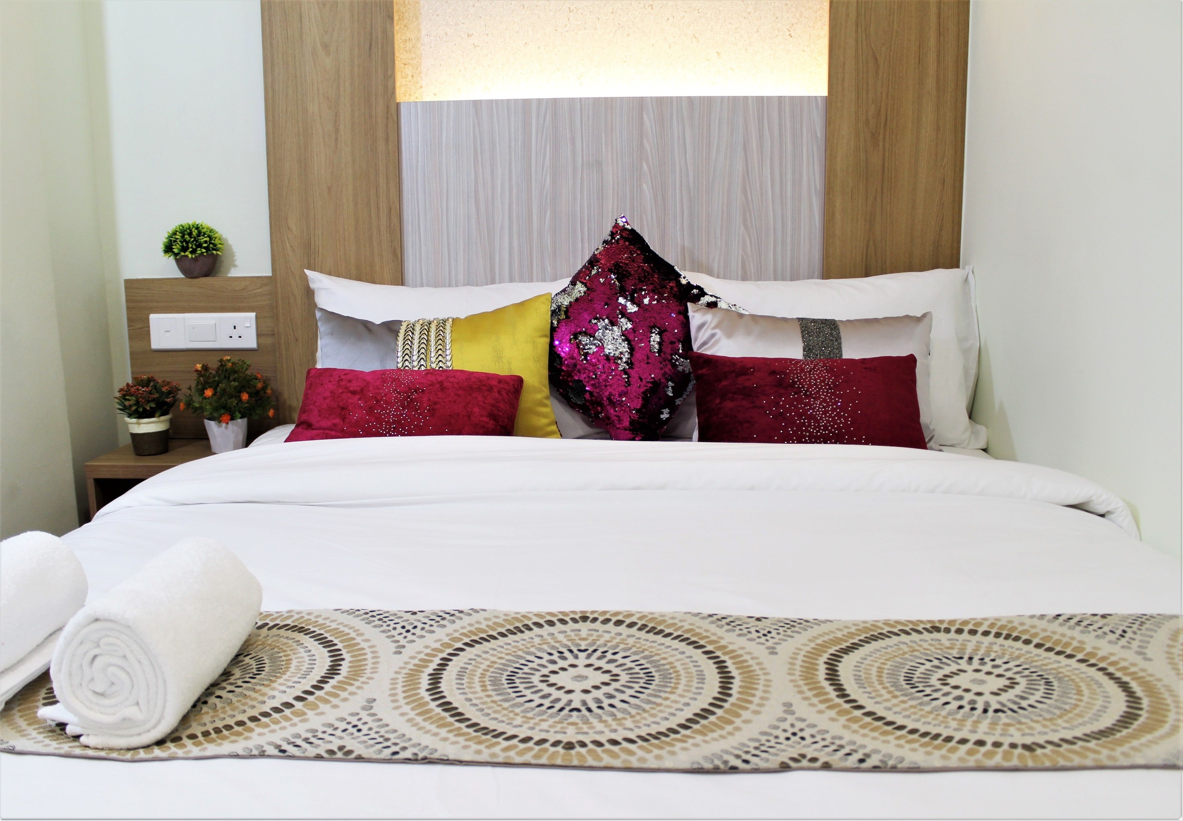 A neatly made bed with white linens, a patterned throw, and multiple pillows in various colors.