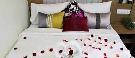 Una cama bien hecha con sábanas blancas, una almohada decorativa y un arreglo floral de rosas sobre la cama.