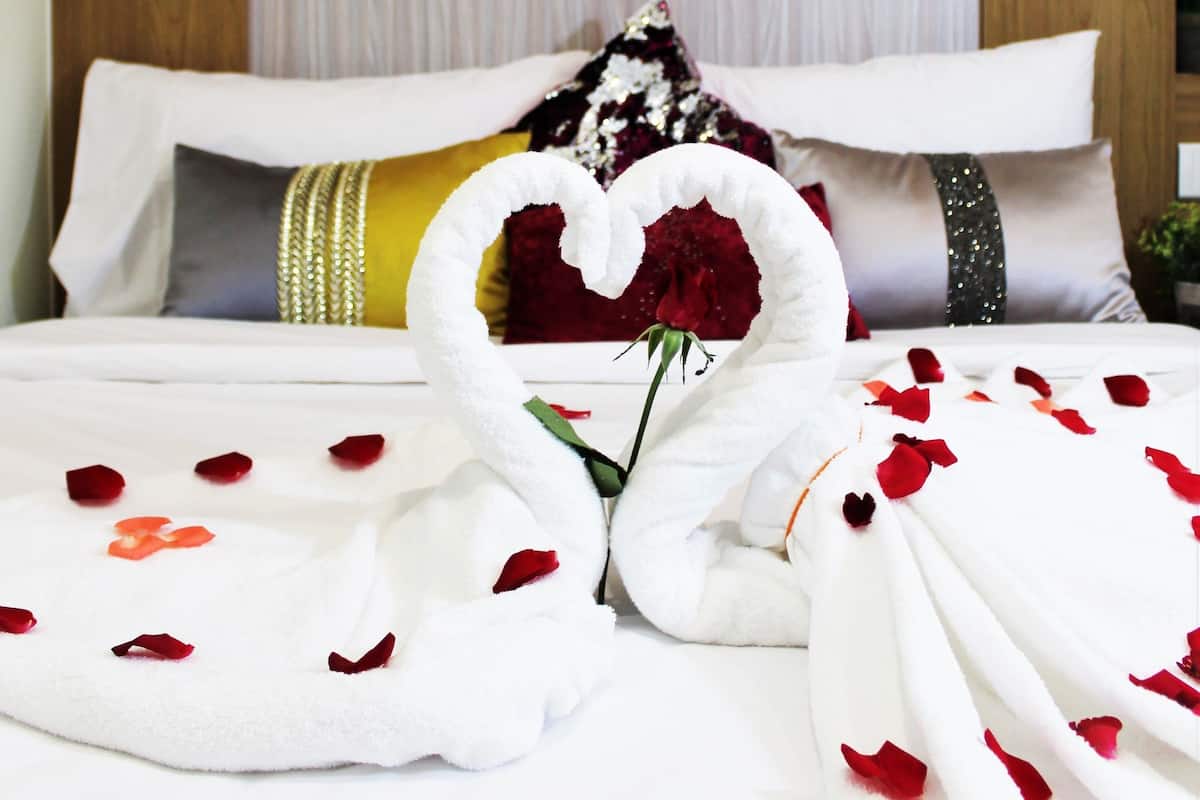 A neatly made bed with rose petals and a heart-shaped towel arrangement.