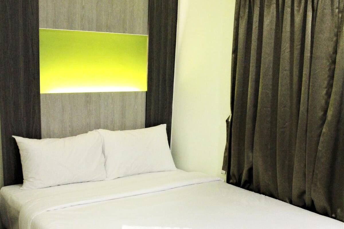 A neatly made bed with white linens, a grey headboard, and a grey curtain.