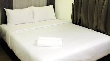 A neatly made bed with white linens, a grey headboard, and a grey curtain.
